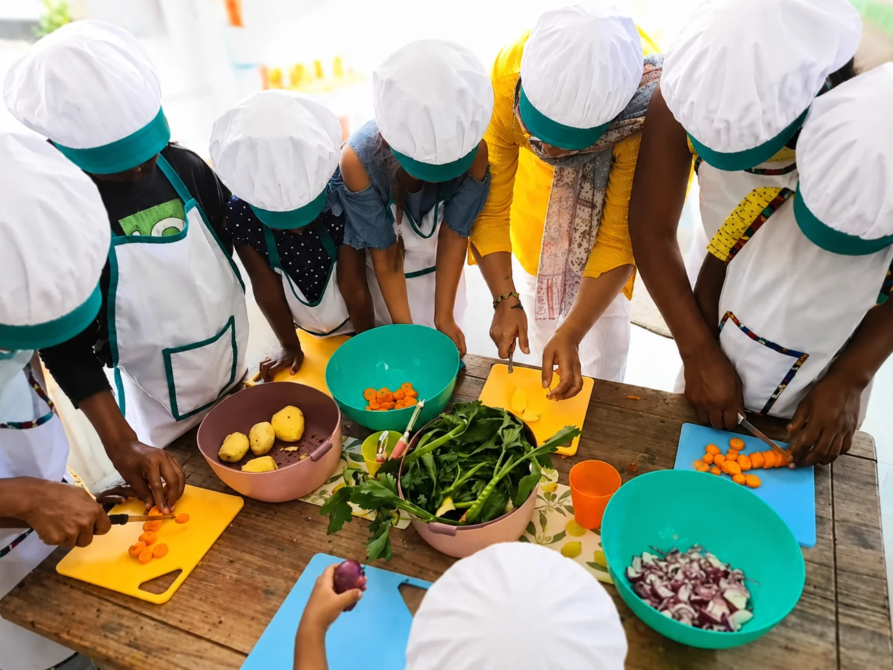 Children in chef hats preparing fresh vegetables together